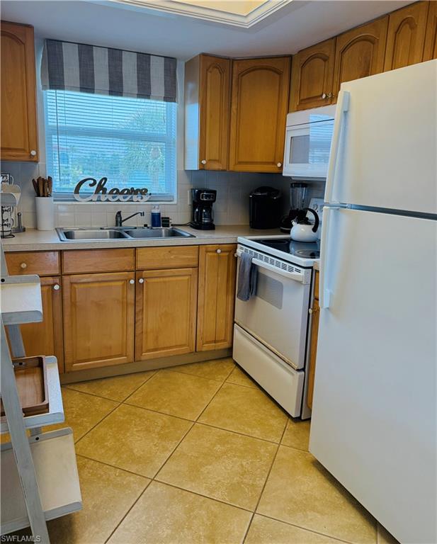 3250 10th Street North, Unit C8 Naples, FL 34103 - Photo 9 of 24 Kitchen featuring wood cabinetry, a double basin stainless steel sink, tile flooring, and white appliances including a refrigerator, range, and microwave