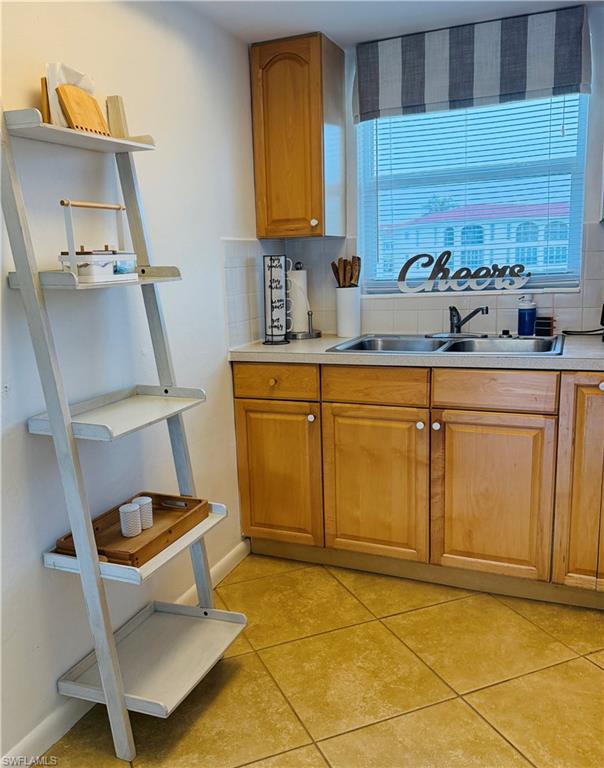 3250 10th Street North, Unit C8 Naples, FL 34103 - Photo 10 of 24 Kitchen area featuring a double basin stainless steel sink, light wood-finish cabinetry, a ceramic tile backsplash, and tile flooring