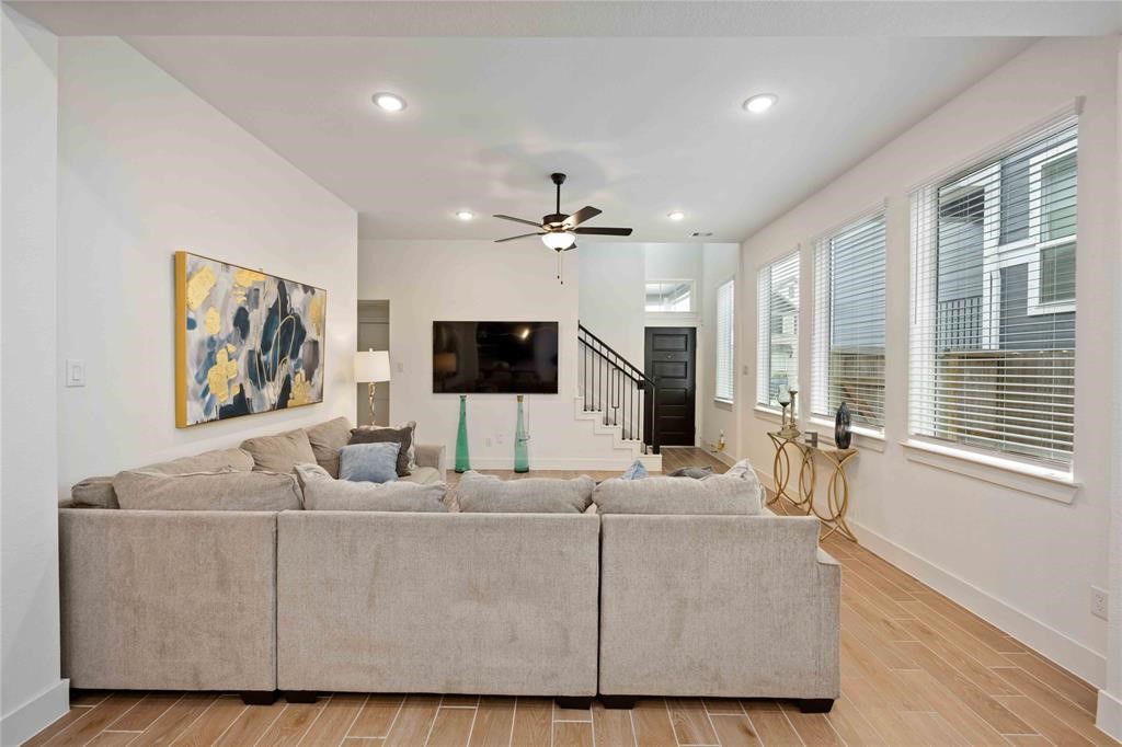 10014 Nectar Path Iowa Colony, TX 77583 - Photo 26 of 26 Bright and inviting living room featuring a large sectional sofa, wall-mounted TV, and ceiling fan. Natural light pours in through multiple windows, highlighting the modern decor and open floor plan.