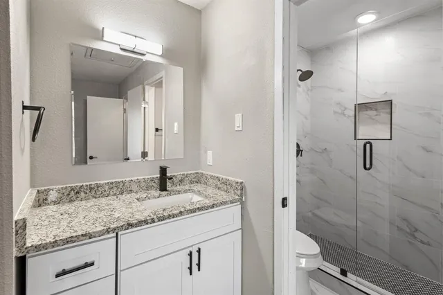 a bathroom with a granite countertop sink a mirror and shower