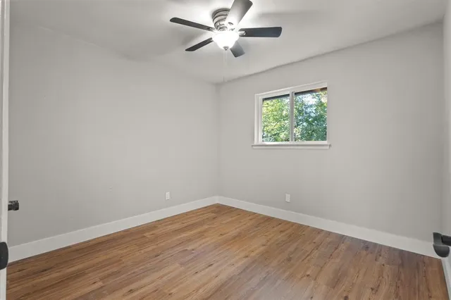an empty room with wooden floor ceiling fan and windows