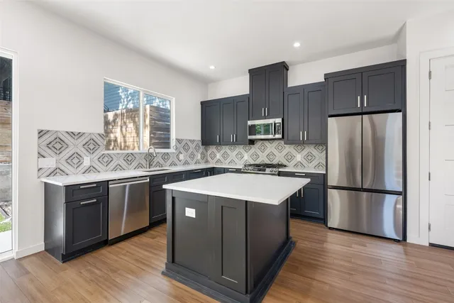 a kitchen with stainless steel appliances granite countertop a refrigerator a sink dishwasher a stove and white cabinets with wooden floor