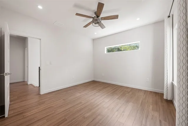 an empty room with wooden floor ceiling fan and windows