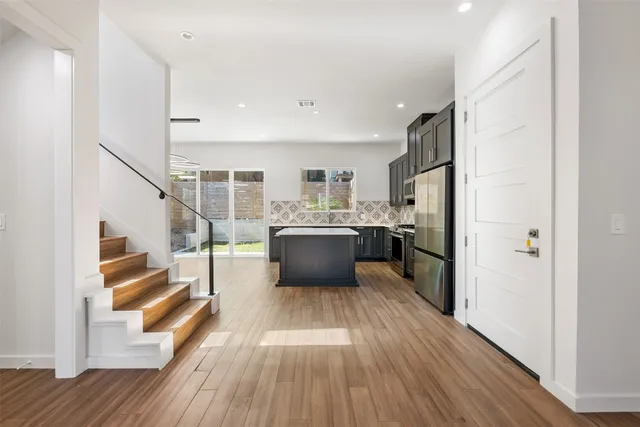 a kitchen with stainless steel appliances a refrigerator a sink dishwasher a stove and white cabinets with wooden floor