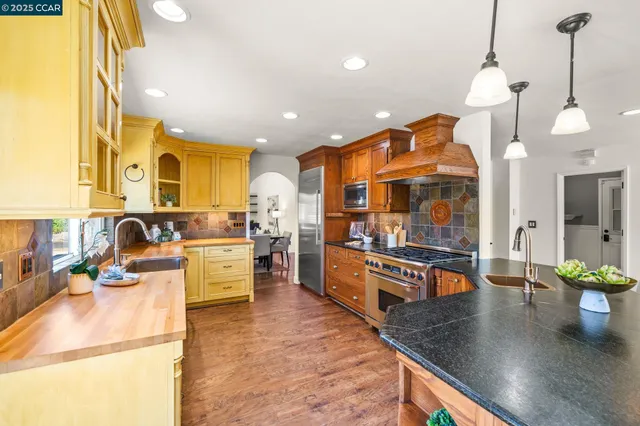 a kitchen with stainless steel appliances granite countertop a sink a stove top oven a counter space and living room view