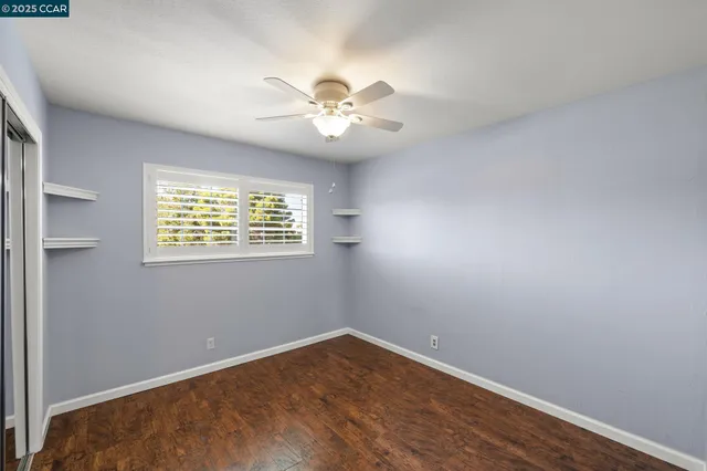 an empty room with wooden floor chandelier fan and windows