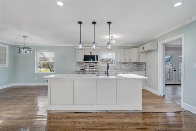 a kitchen with stainless steel appliances granite countertop a sink a stove and white cabinets with wooden floor
