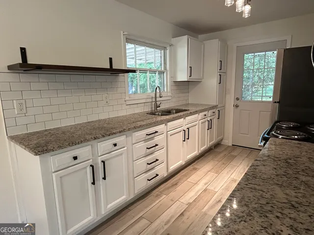 a kitchen with granite countertop a sink stainless steel appliances white cabinets and a window