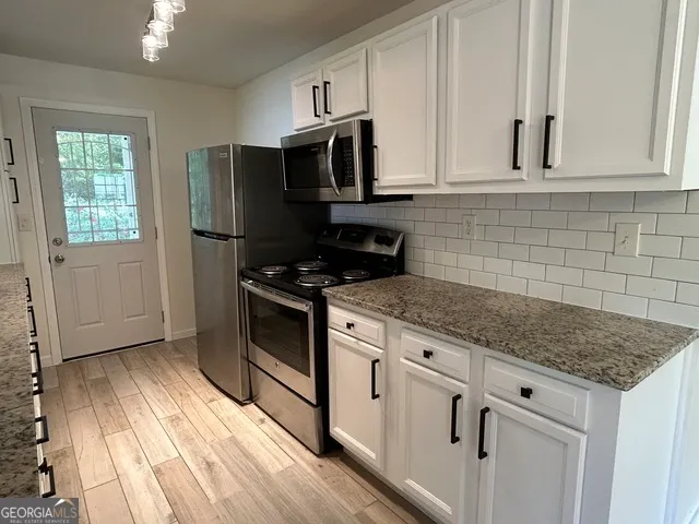 a kitchen with granite countertop white cabinets stainless steel appliances a sink and a window