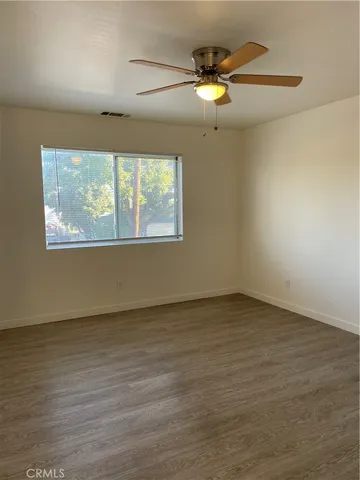 an empty room with wooden floor fan and windows