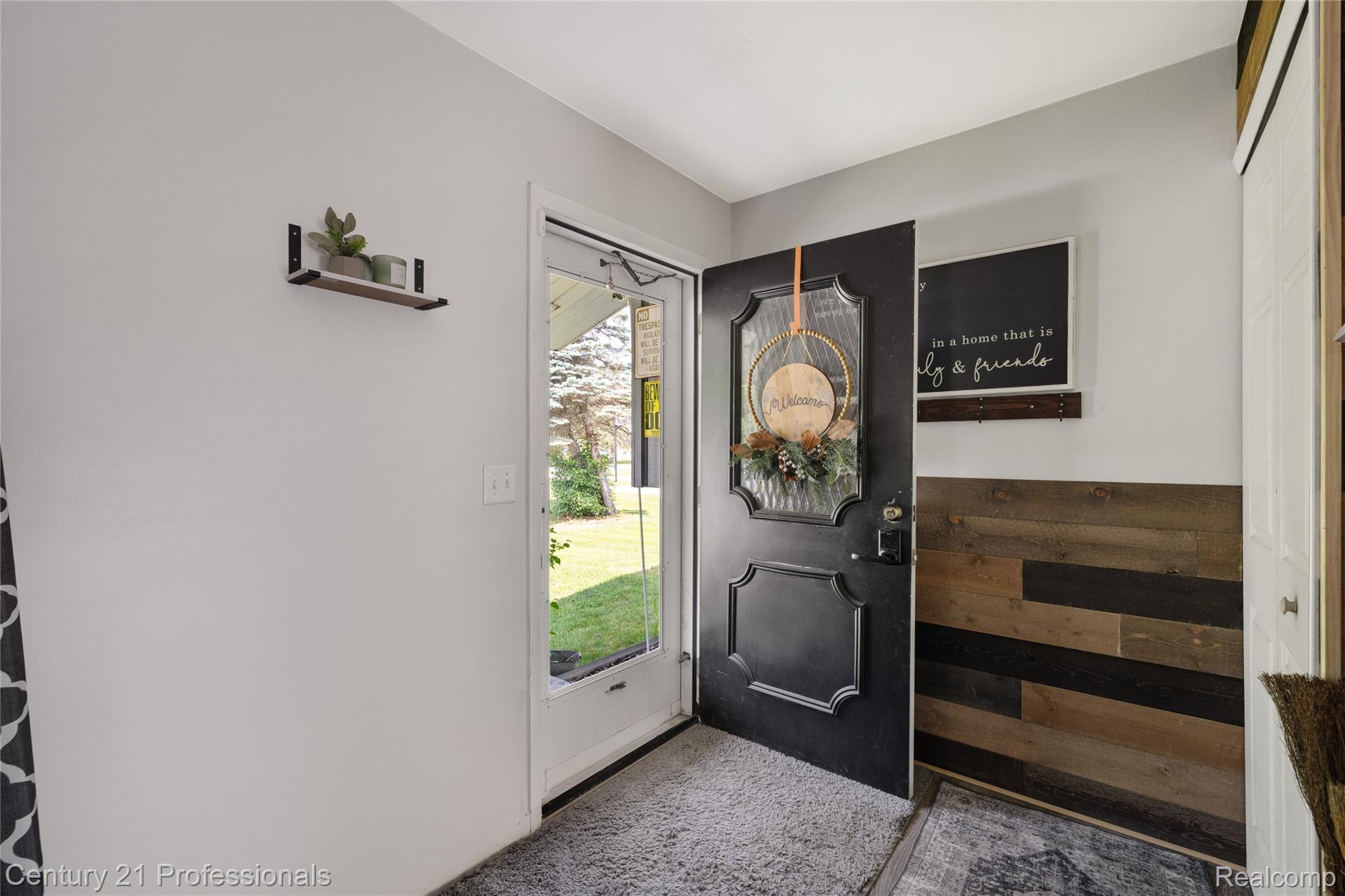 15037 Hogan Road Linden, MI 48451 - Photo 3 of 38 Entryway featuring a black paneled door with glass insert, wood-finish accent wall paneling, and light gray wall paint