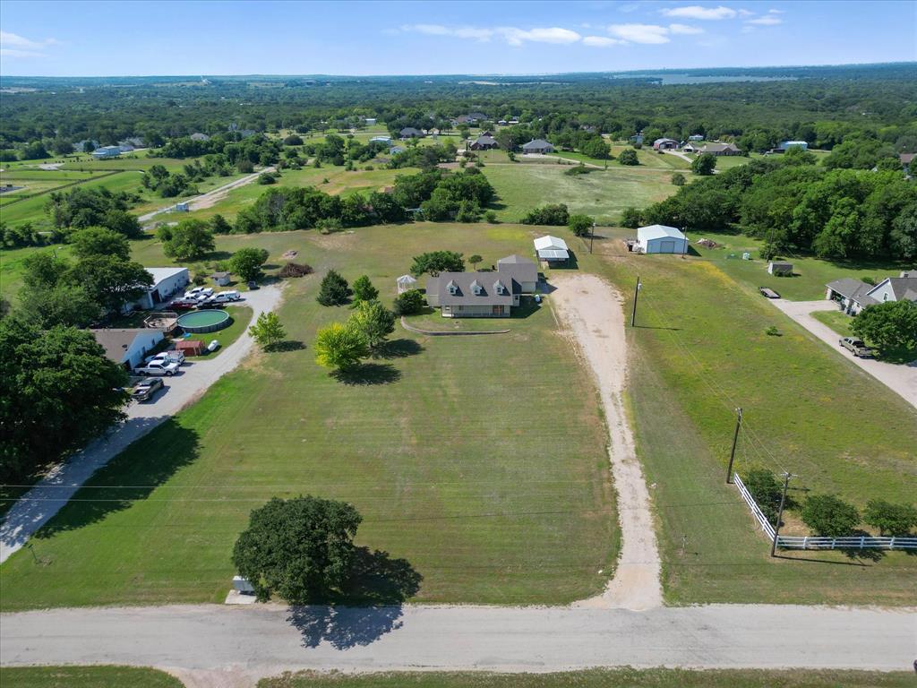 289 County Road 4655 Rhome, TX 76078 - Photo 33 of 34 Expansive land parcel featuring a residential structure, a gravel driveway, two outbuildings, and mature trees, all set within a verdant landscape