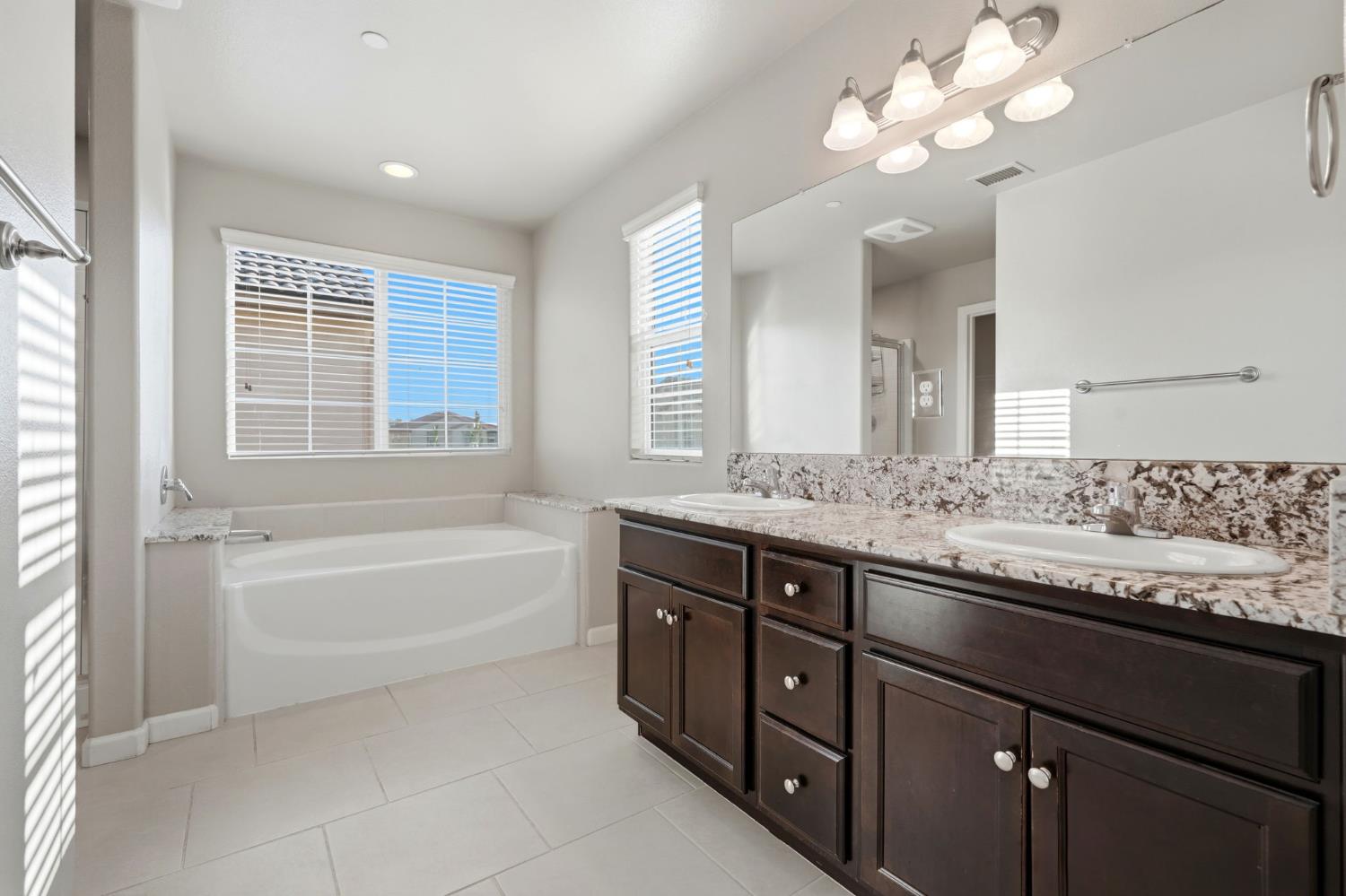 1515 Zenith Clovis, CA 93619 - Photo 35 of 41 a bathroom with a granite countertop bathtub a double vanity sink a vanity a lamp and a mirror