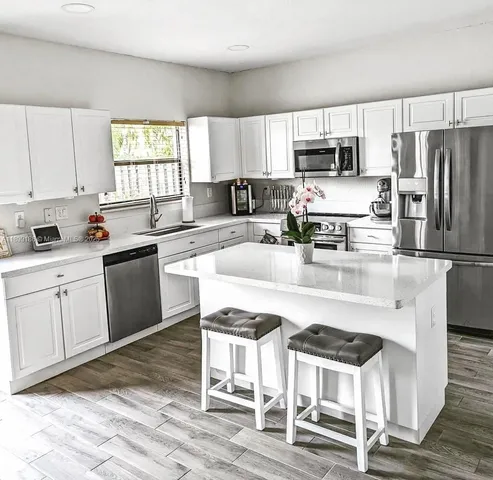 a kitchen with stainless steel appliances granite countertop a stove a sink dishwasher a refrigerator and white cabinets with wooden floor