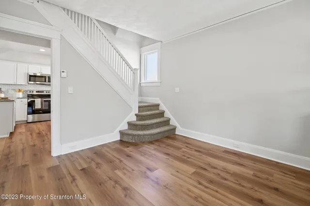 a view of empty room with wooden floor and kitchen view