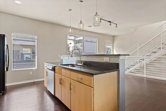 a kitchen with stainless steel appliances granite countertop a refrigerator a sink dishwasher a stove and white countertops with wooden floor