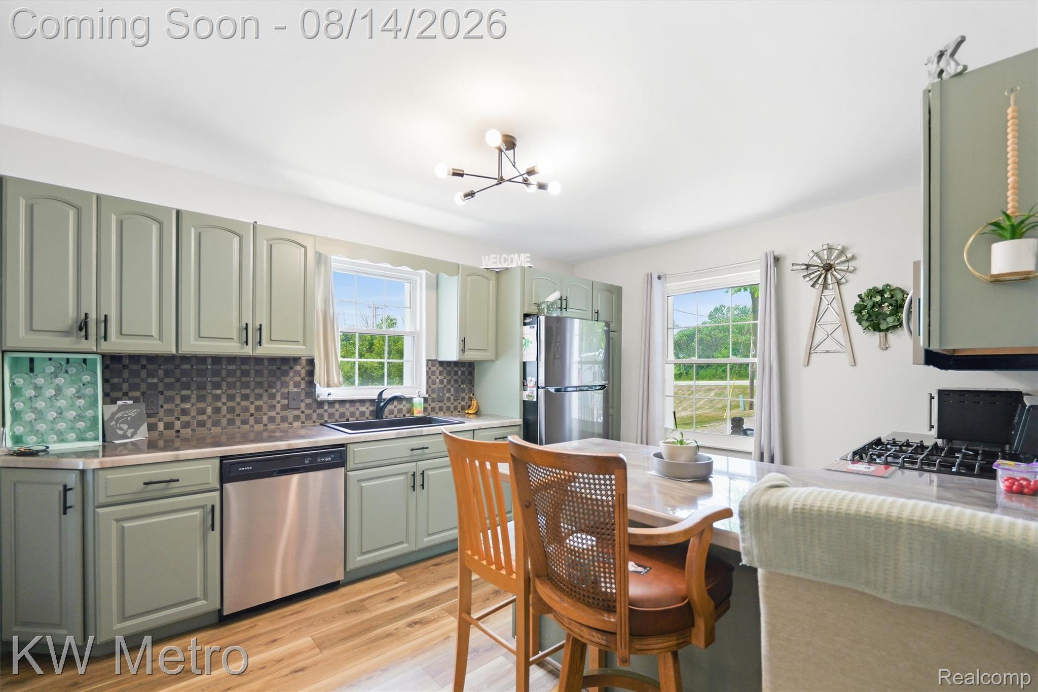 201 South Maple Leaf Road Lapeer, MI 48446 - Photo 4 of 70 Kitchen featuring light green cabinetry, stainless steel dishwasher, black faucet, tile backsplash, and light wood-finish flooring