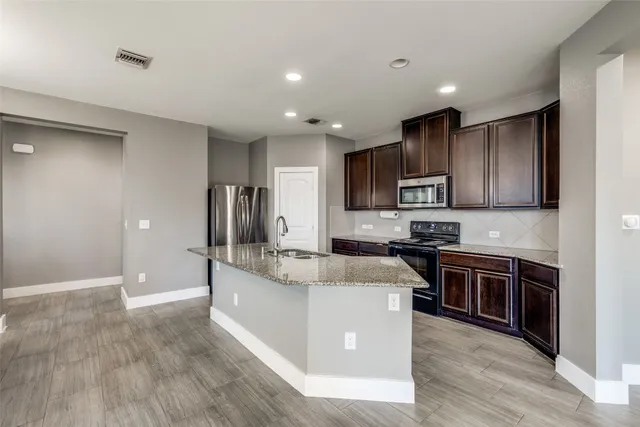 a large kitchen with stainless steel appliances granite countertop a stove top oven a sink dishwasher a refrigerator and cabinets with wooden floor