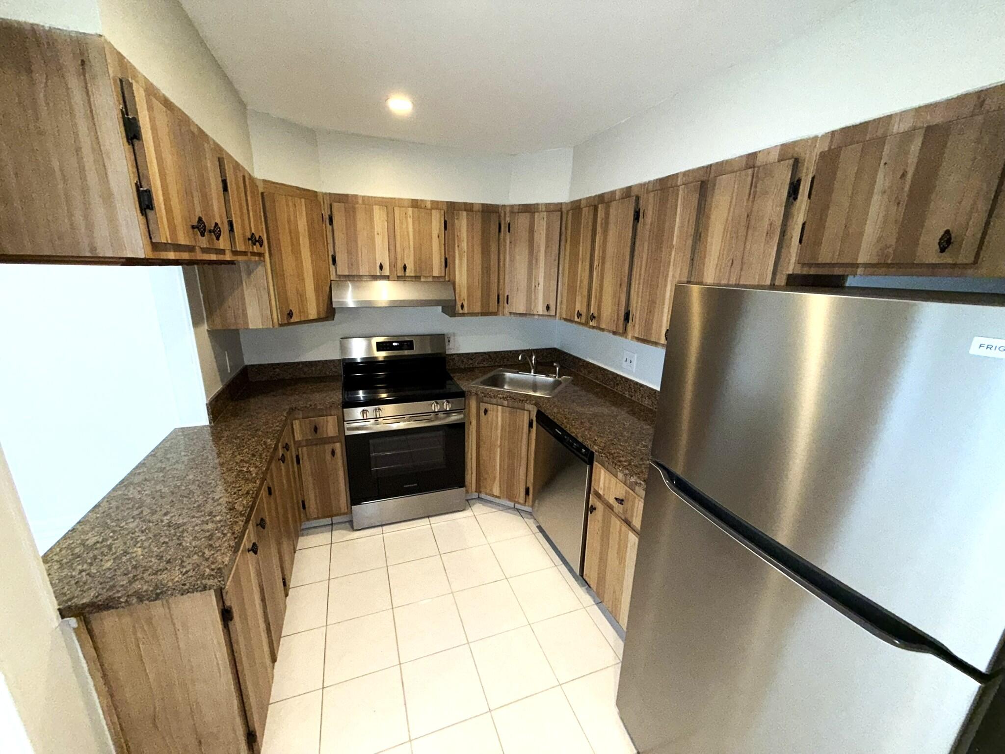 4987 Sable Pine Circle, Unit B2 West Palm Beach, FL 33417 - Photo 3 of 12 a kitchen with granite countertop a refrigerator a sink and wooden cabinets