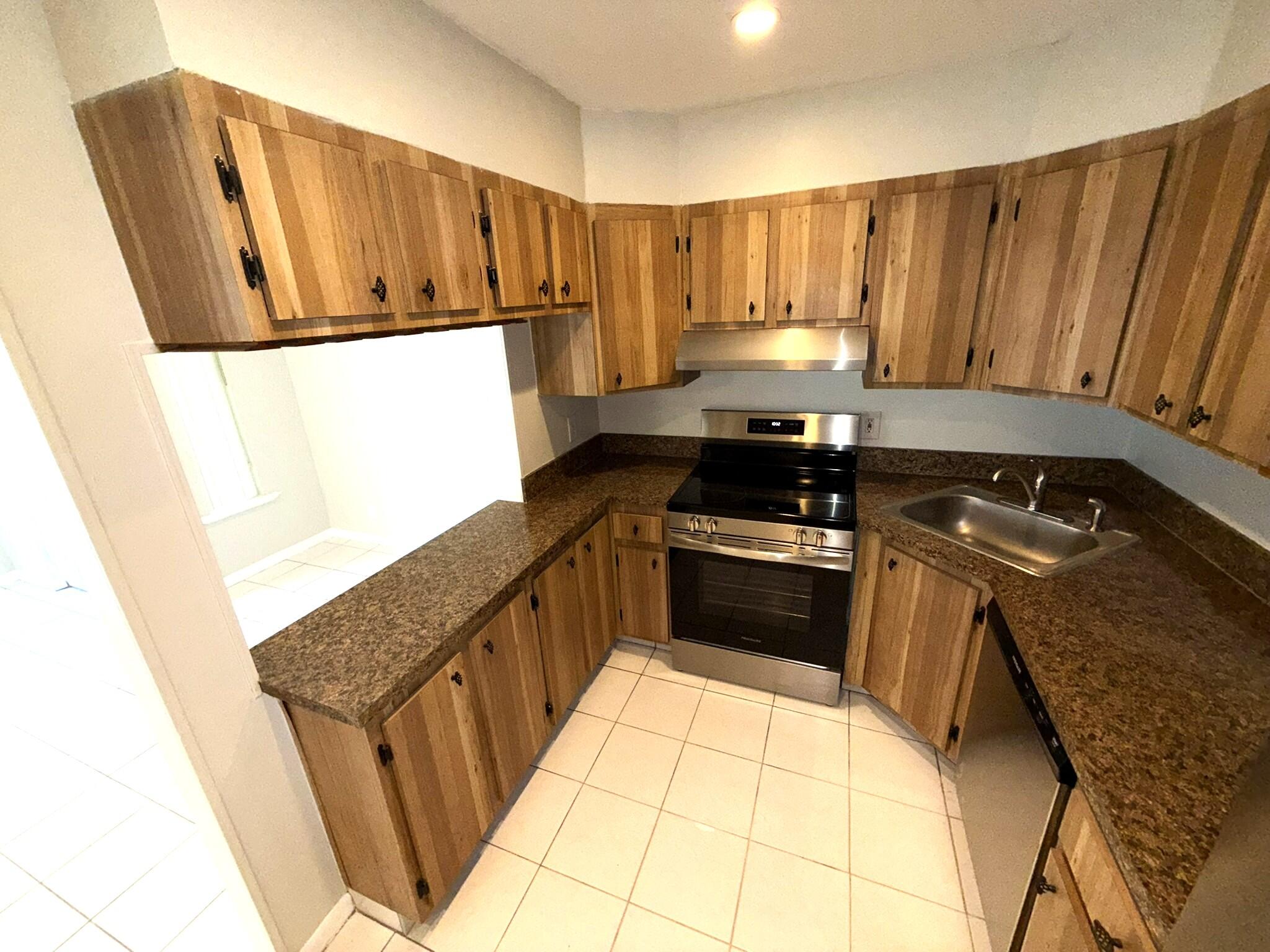 4987 Sable Pine Circle, Unit B2 West Palm Beach, FL 33417 - Photo 4 of 12 a kitchen with granite countertop a refrigerator a stove a sink a washer and dryer