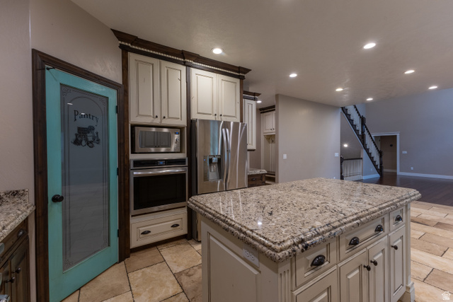 3565 West 1350th Street North Vernal, UT 84078 - Photo 13 of 54 Kitchen featuring a large island with stone countertop, stainless steel appliances, light-toned cabinetry, a turquoise pantry door with frosted glass, and stone-look tile flooring