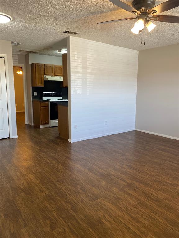 an empty room with wooden floor kitchen view and a window