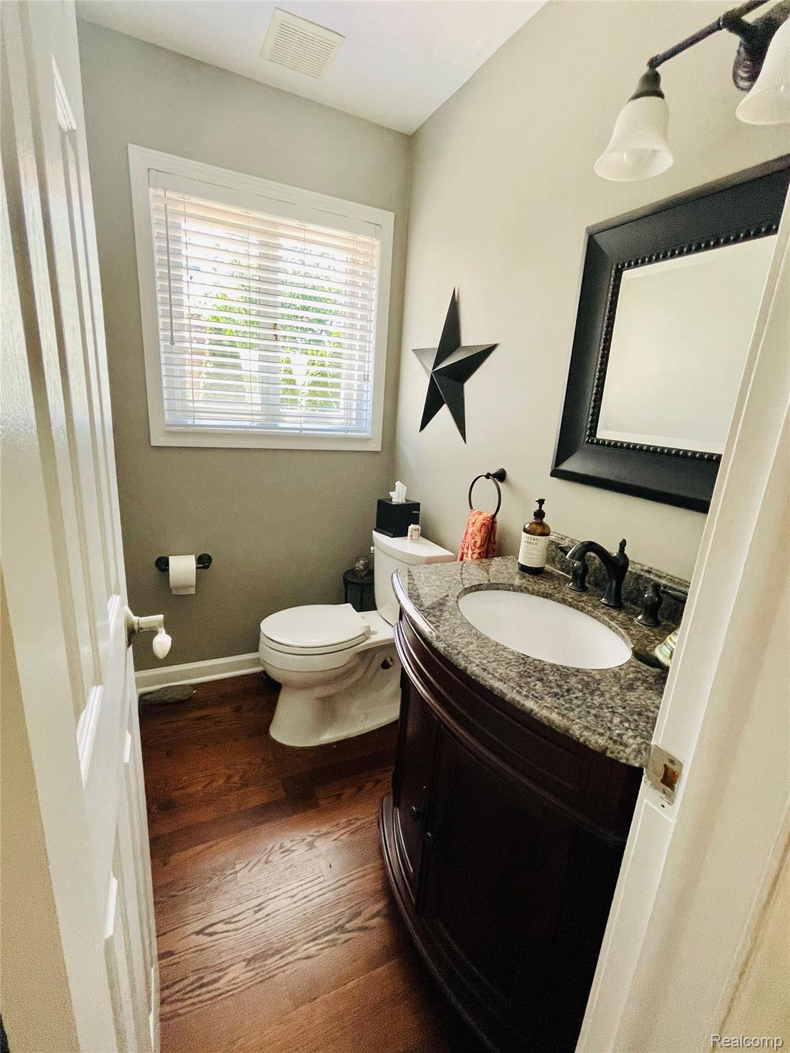 488 Welch Road Northville, MI 48167 - Photo 8 of 22 Powder room with wood-finish flooring, a dark wood-finish vanity with a granite countertop and undermount sink, a white toilet, and a window with blinds