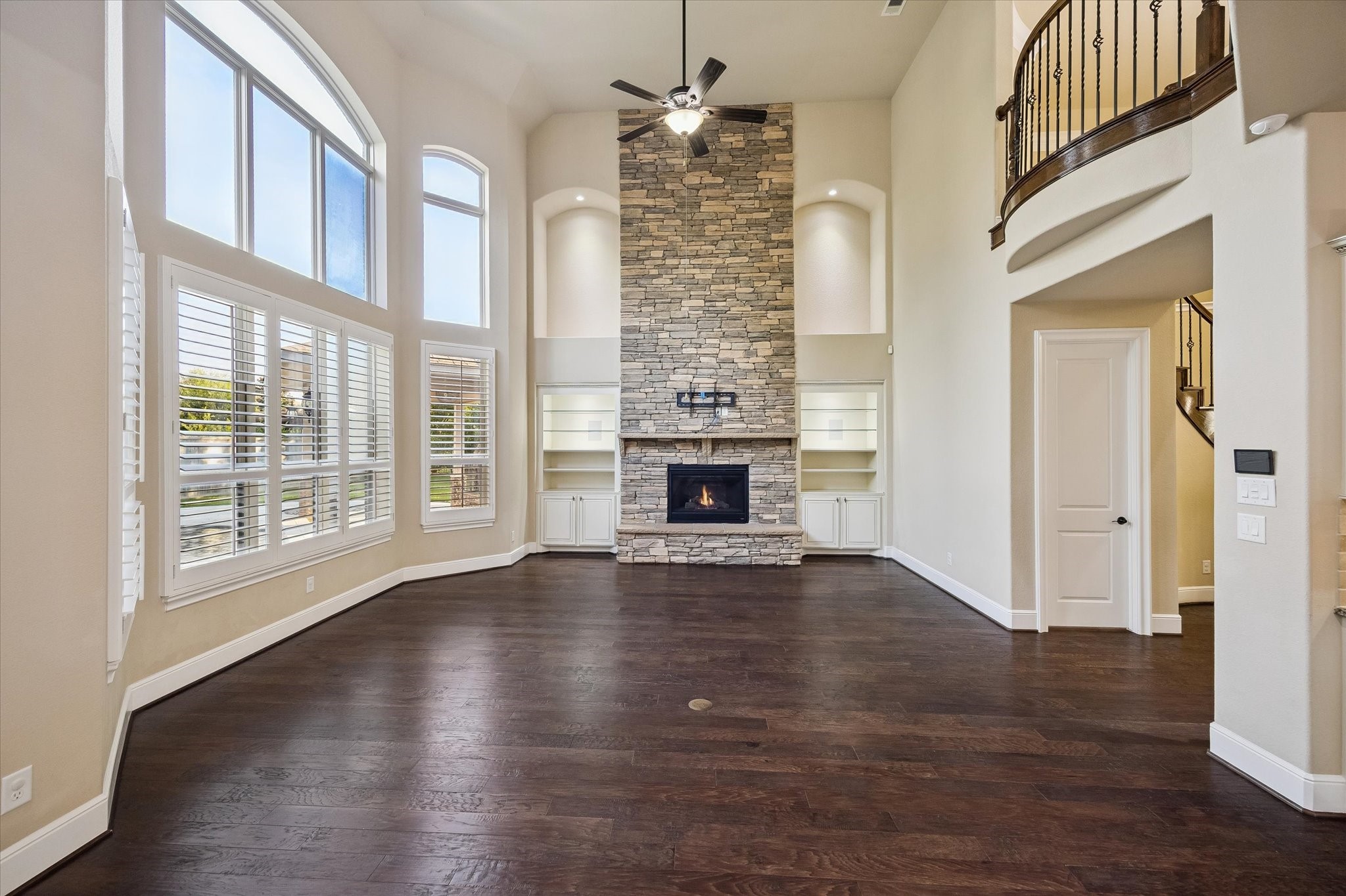 35 North Fremont Ridge Loop Spring, TX 77389 - Photo 7 of 37 Bathed in natural light, the grand living room features soaring ceilings, rich hardwood floors, expansive windows with plantation shutters, and a striking floor-to-ceiling stone fireplace, creating a warm yet sophisticated gathering space.