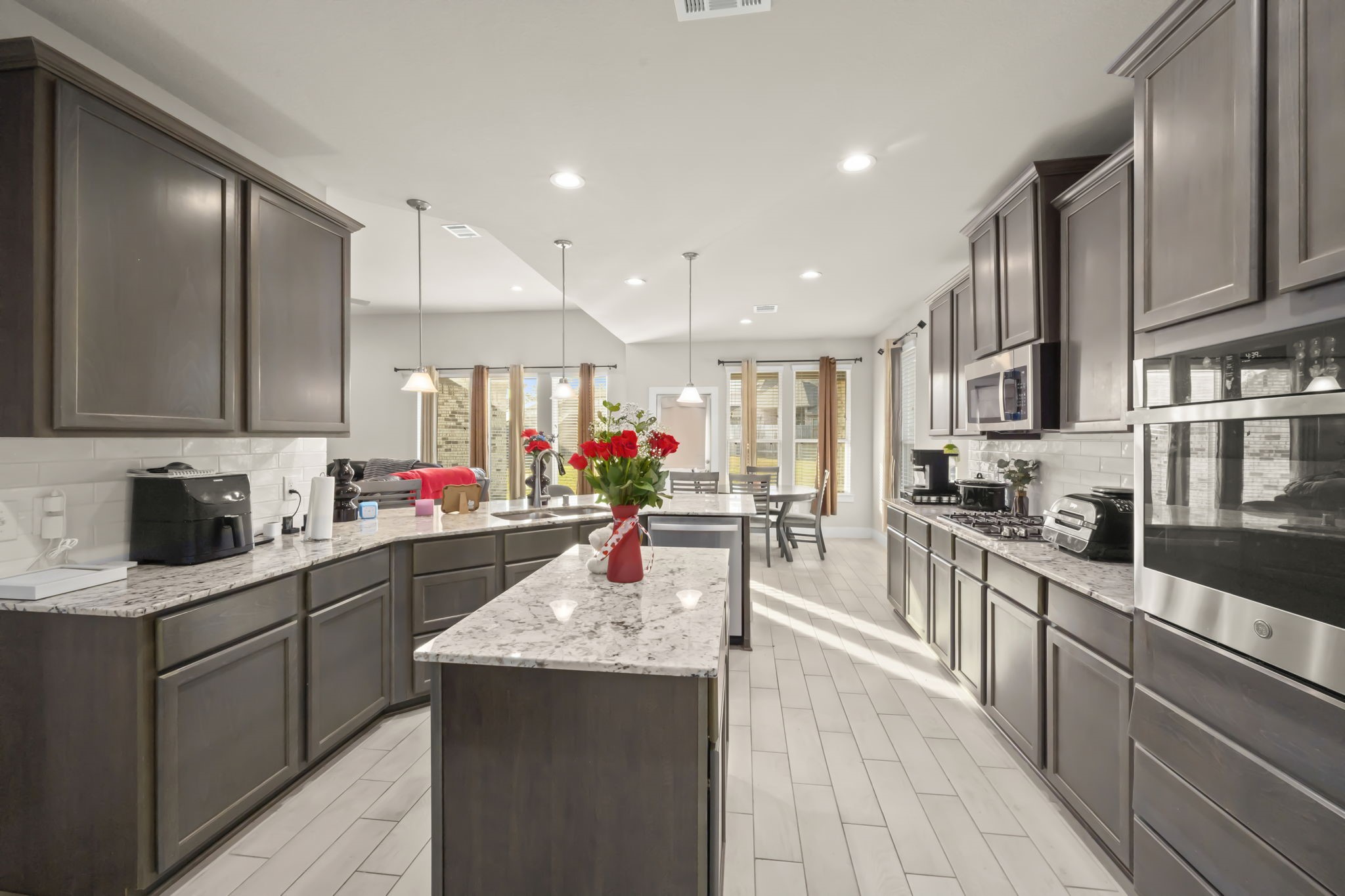 24715 Native Forest Spring, TX 77373 - Photo 12 of 37 This modern kitchen features sleek dark cabinets, a central island with granite countertops, and stainless steel appliances. The open layout connects to a bright dining area with large windows, providing ample natural light.