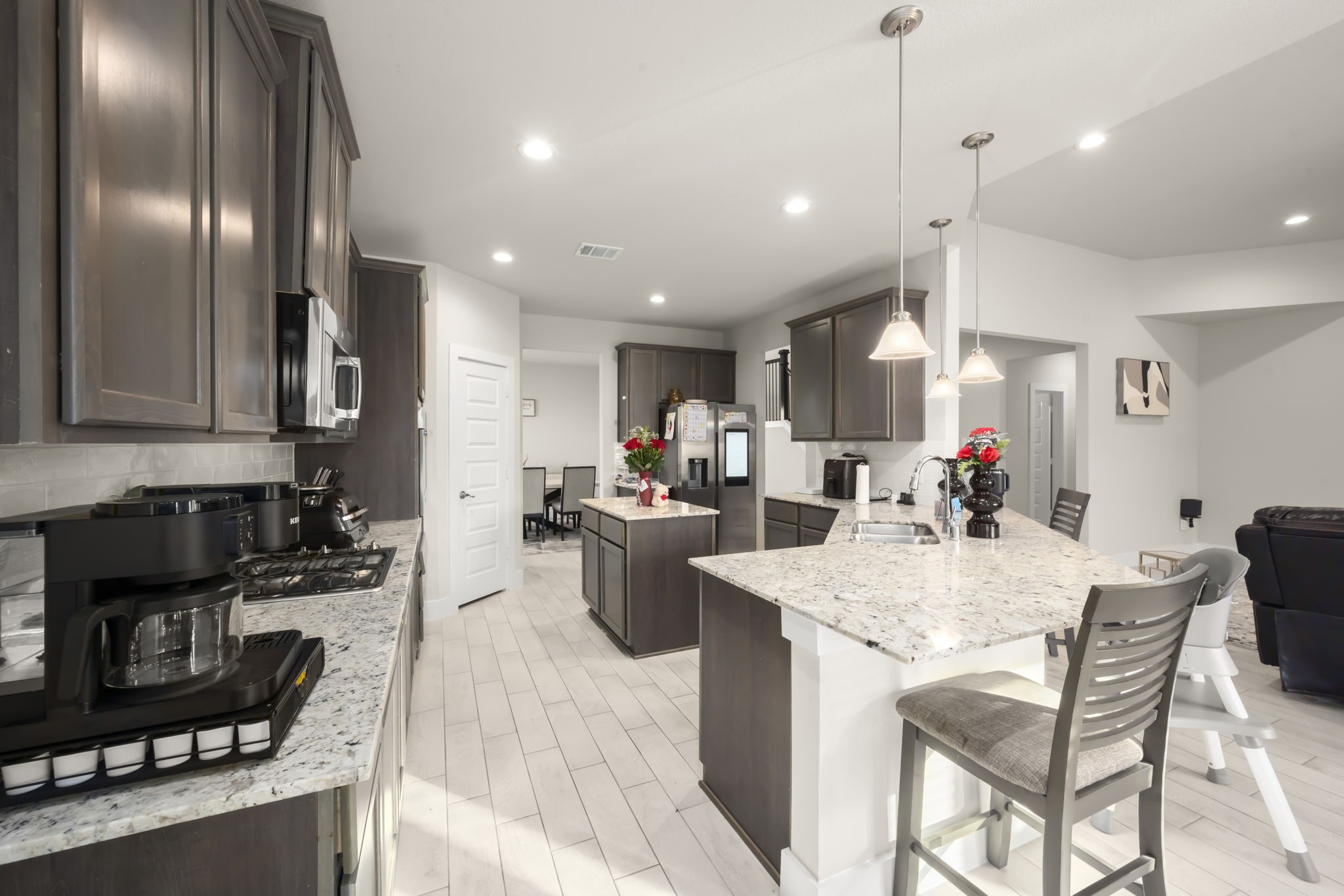 24715 Native Forest Spring, TX 77373 - Photo 13 of 37 This modern kitchen features sleek dark cabinetry, granite countertops, and stainless steel appliances. It includes a spacious island with bar seating and pendant lighting, offering a bright and inviting space for cooking and entertaining.