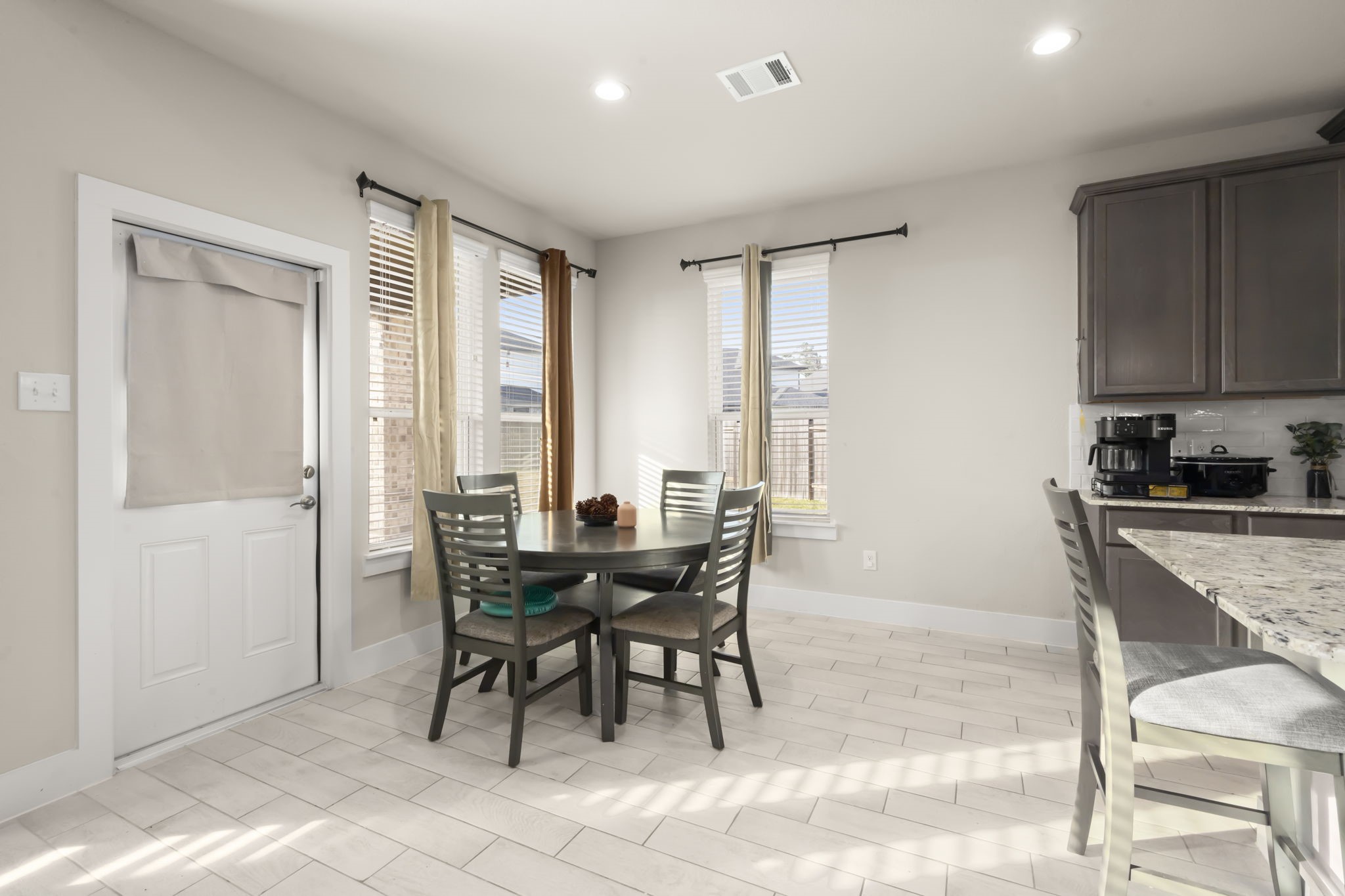 24715 Native Forest Spring, TX 77373 - Photo 14 of 37 Bright and welcoming dining area with large windows, modern tile flooring, and a cozy table for four. The space connects to a kitchen with sleek cabinetry and a granite countertop, creating an inviting atmosphere for meals and gatherings.