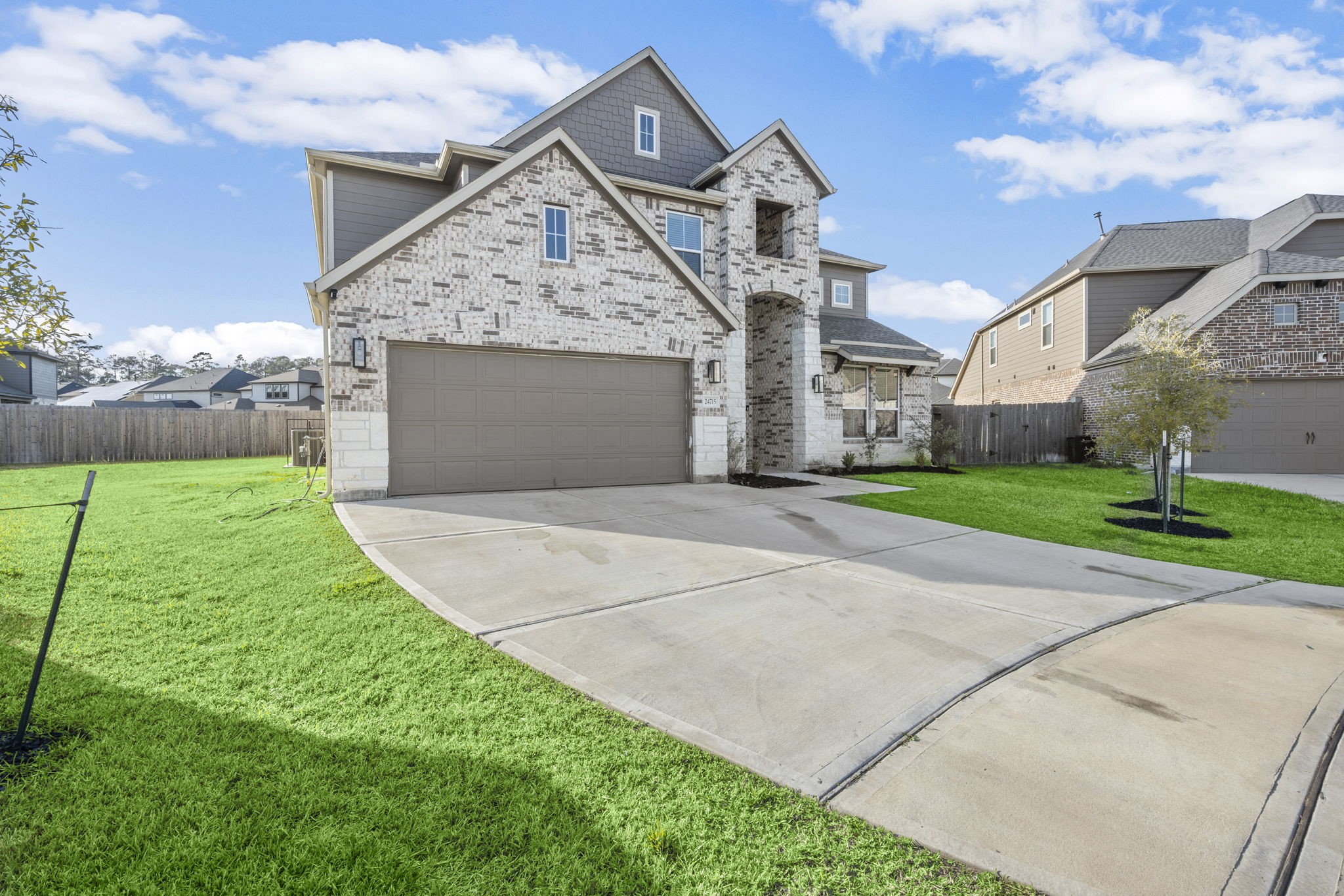 24715 Native Forest Spring, TX 77373 - Photo 2 of 37 This photo shows a modern, two-story brick house with a spacious two-car garage. The well-maintained lawn and long driveway enhance its curb appeal in a suburban neighborhood setting.