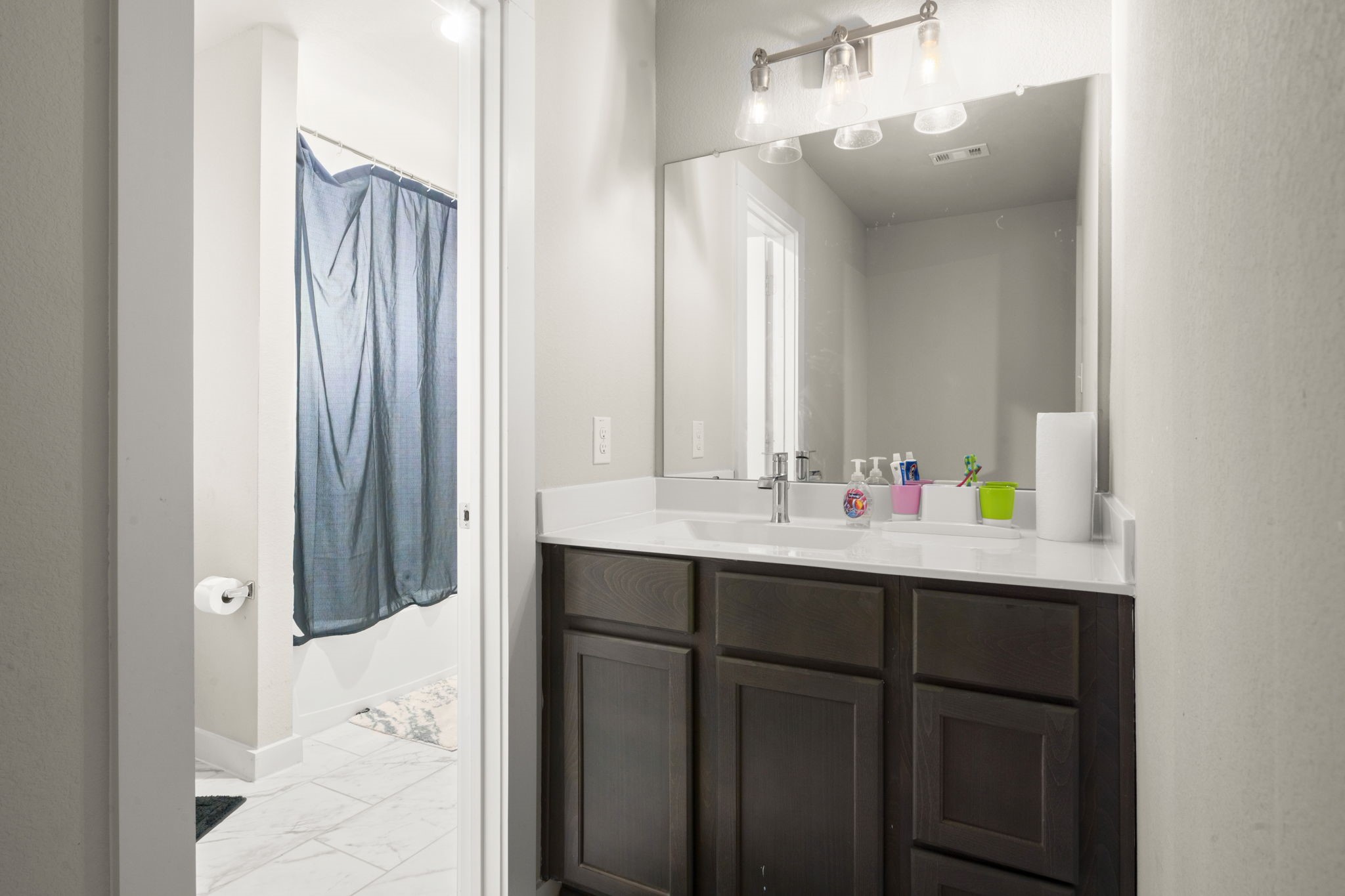 24715 Native Forest Spring, TX 77373 - Photo 25 of 37 This bathroom features a modern design with a large mirror, stylish vanity with dark wood cabinets, bright lighting, and a shower area with a curtain. The neutral color palette adds a clean, contemporary feel.