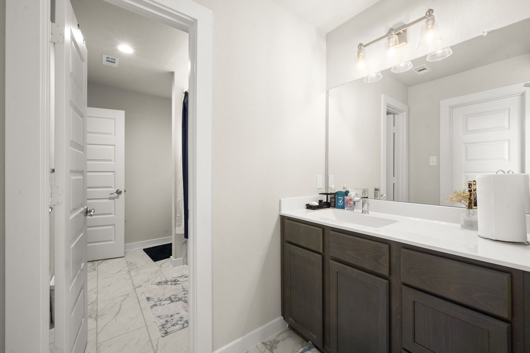 24715 Native Forest Spring, TX 77373 - Photo 27 of 37 This photo showcases a modern bathroom with a spacious vanity featuring dark wood cabinets and a large mirror. The room has clean, white walls and doors, and the floor is finished with elegant marble tiles. Bright lighting adds to the fresh and inviting atmosphere.