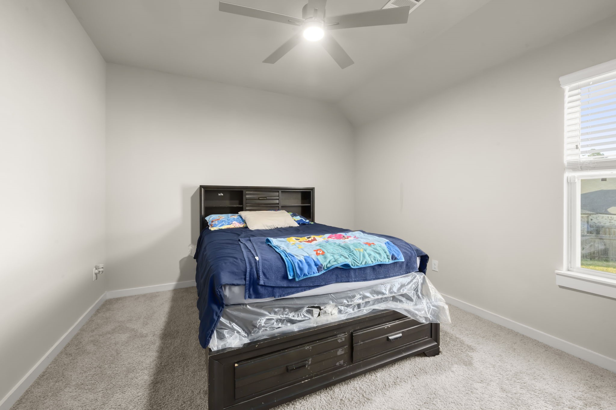 24715 Native Forest Spring, TX 77373 - Photo 29 of 37 This is a cozy bedroom featuring carpeted flooring, neutral walls, and a ceiling fan. It has a window for natural light and a bed with built-in storage drawers, offering space and functionality.