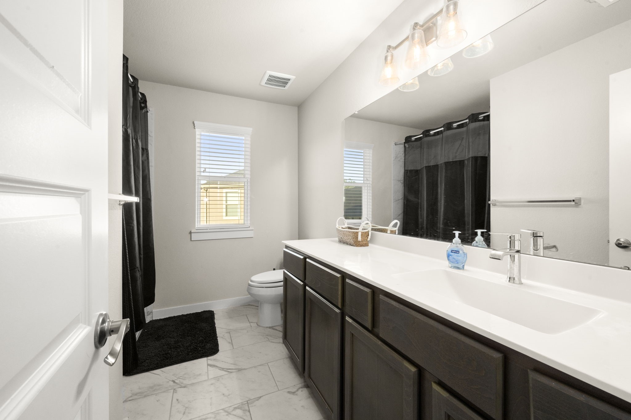 24715 Native Forest Spring, TX 77373 - Photo 30 of 37 Bright and modern bathroom with a double vanity, large mirror, and ample lighting. Features a bathtub with a dark curtain, tiled floor, and a window for natural light.
