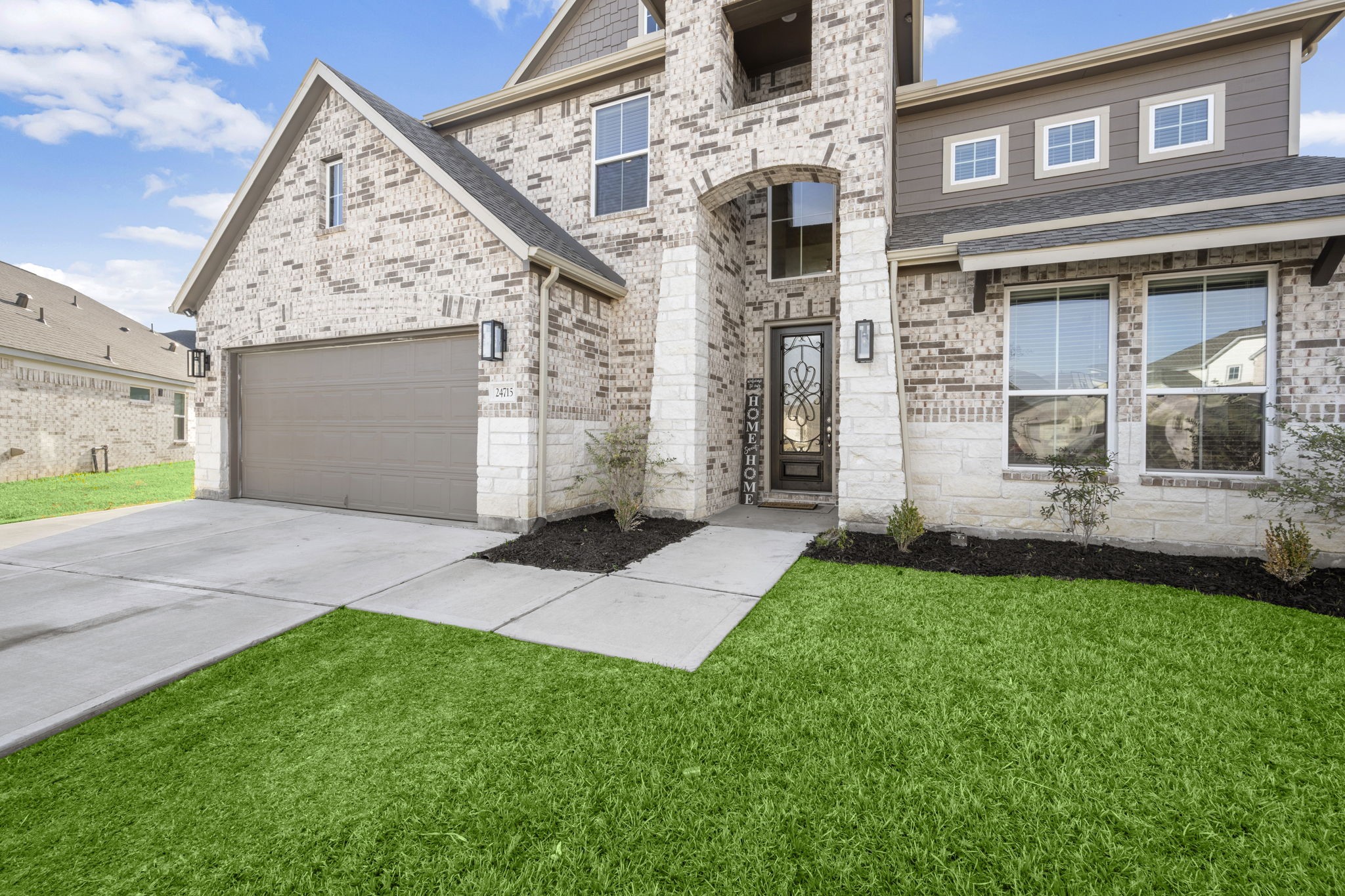 24715 Native Forest Spring, TX 77373 - Photo 4 of 37 This photo showcases a modern two-story brick home with a spacious driveway leading to a two-car garage. The entrance features an elegant arched doorway, and the property is complemented by a well-maintained lawn and simple landscaping.