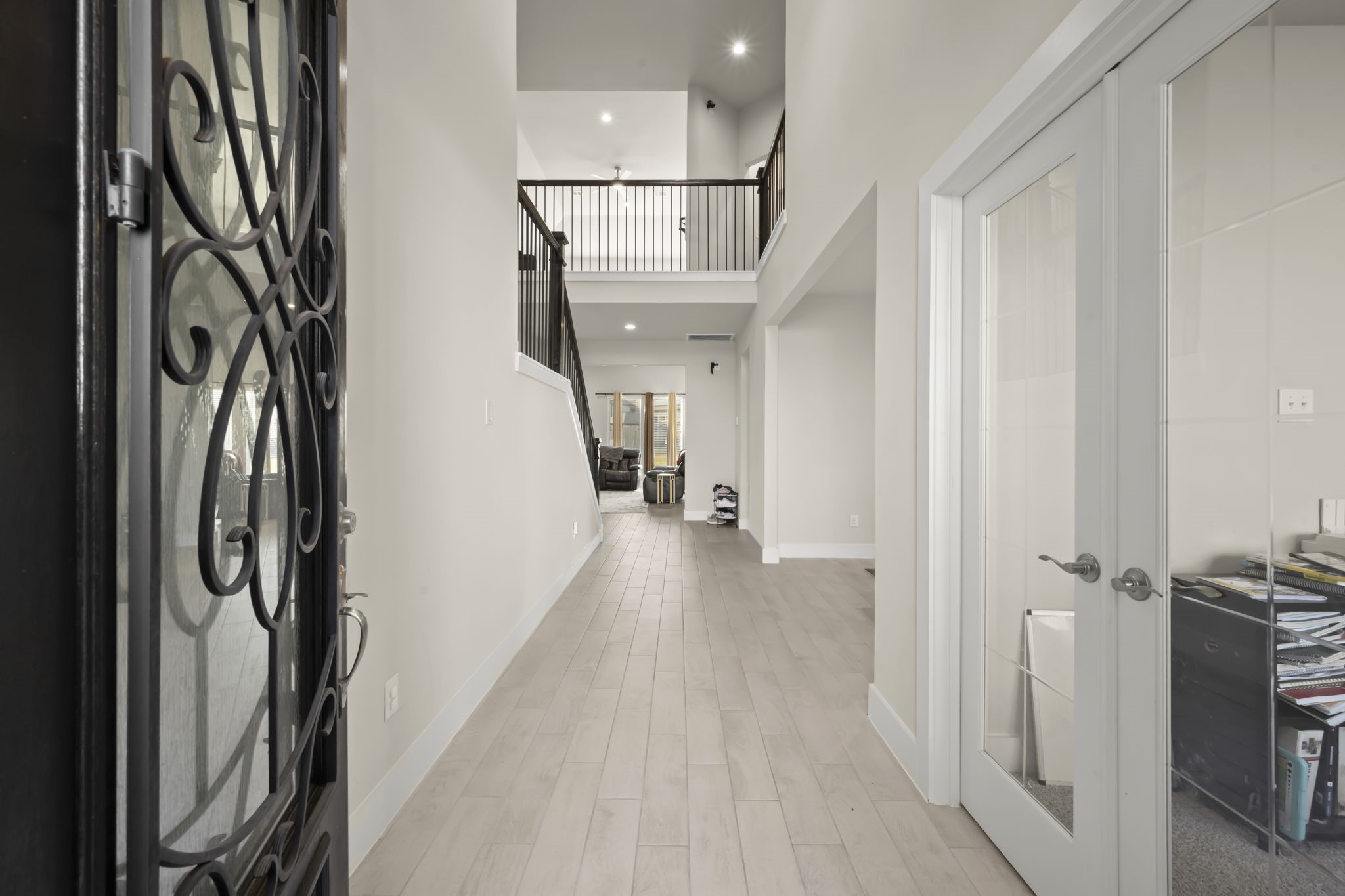 24715 Native Forest Spring, TX 77373 - Photo 5 of 37 This photo showcases a modern entryway with high ceilings, light wood flooring, and a wrought iron front door. The hallway leads to a spacious living area, and there's a room with glass French doors on the right.