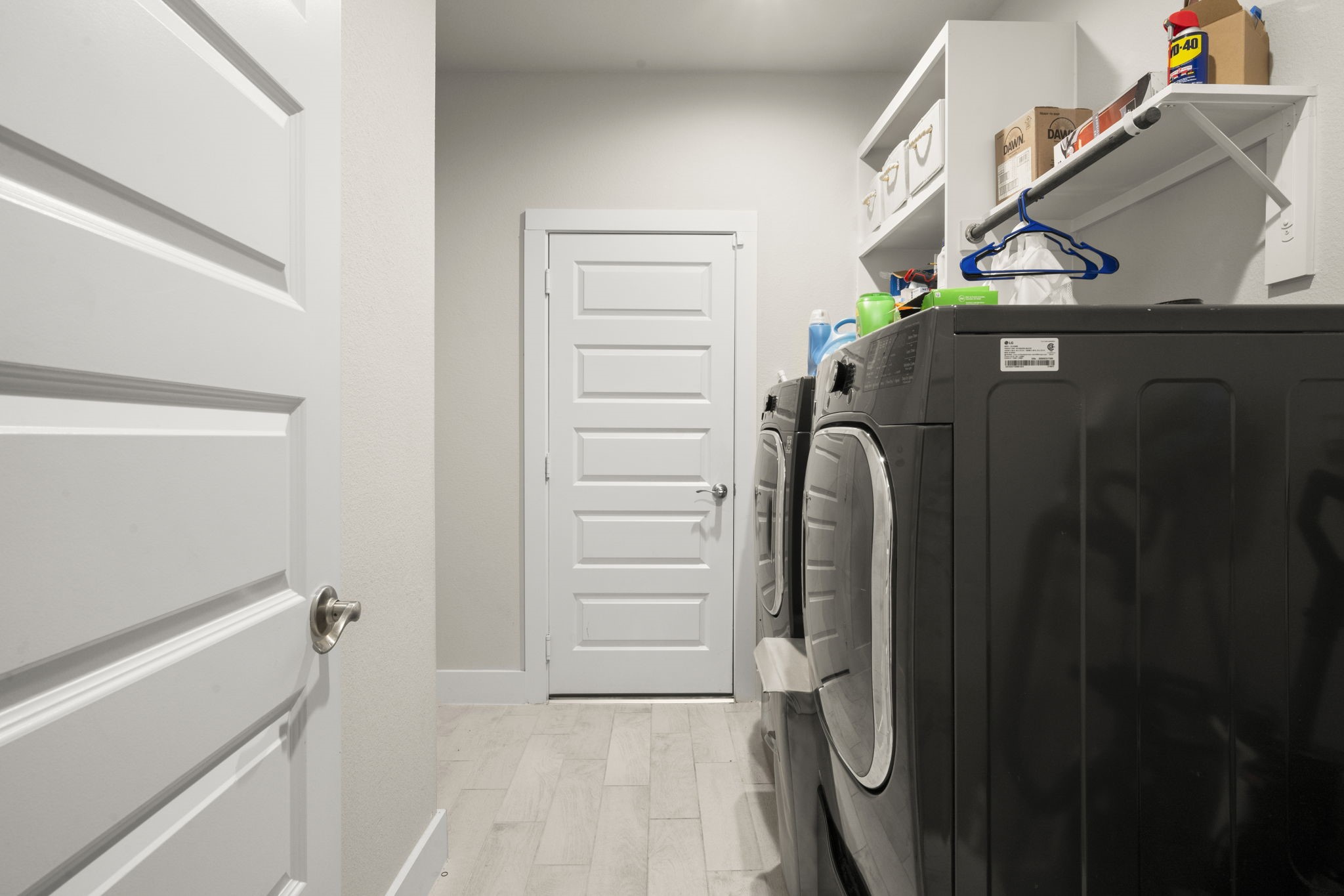 24715 Native Forest Spring, TX 77373 - Photo 10 of 37 This photo shows a compact laundry room with modern appliances, white shelving for storage, and a light wood floor, offering functionality and organization.