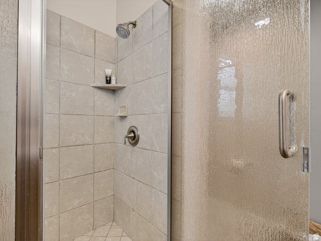 557 Craftsman Way Midway, UT 84049 - Photo 28 of 59 Shower enclosure featuring textured glass, brushed nickel fixtures, a built-in corner shelf, and neutral-toned wall tiling