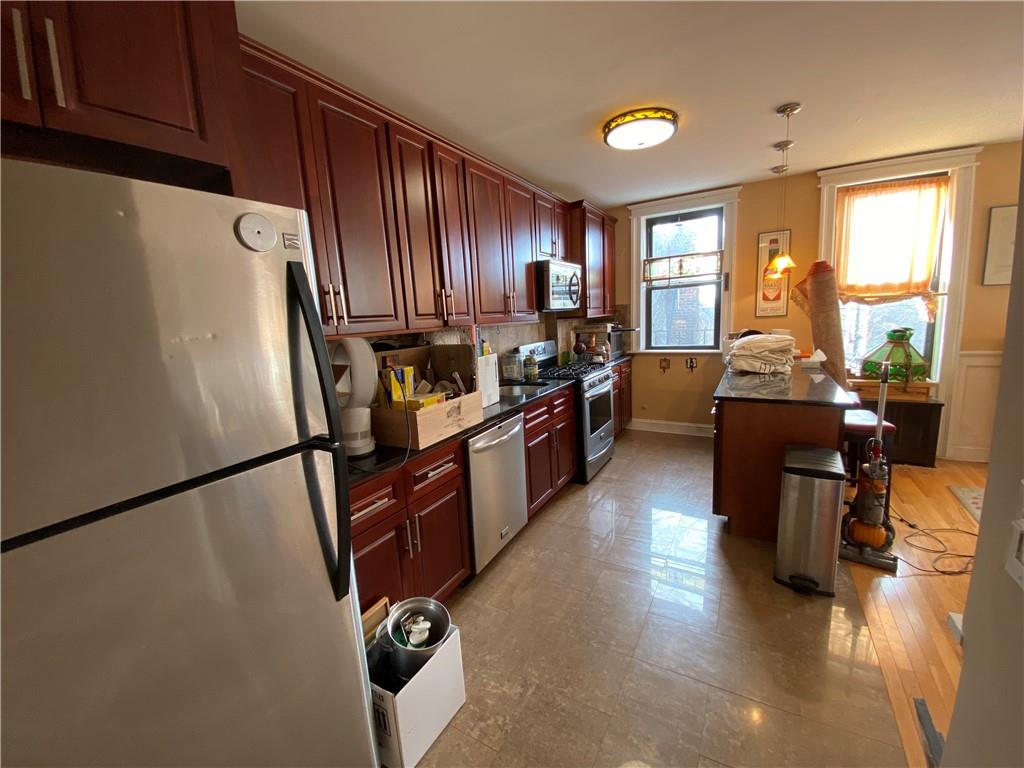 7912 3rd Avenue Brooklyn, NY 11209 - Photo 8 of 18 a kitchen with granite countertop a refrigerator a stove a sink dishwasher and a dining table with wooden cabinet