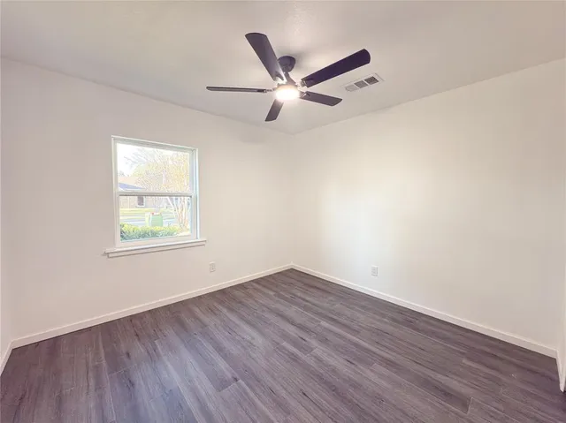 an empty room with wooden floor ceiling fan and windows