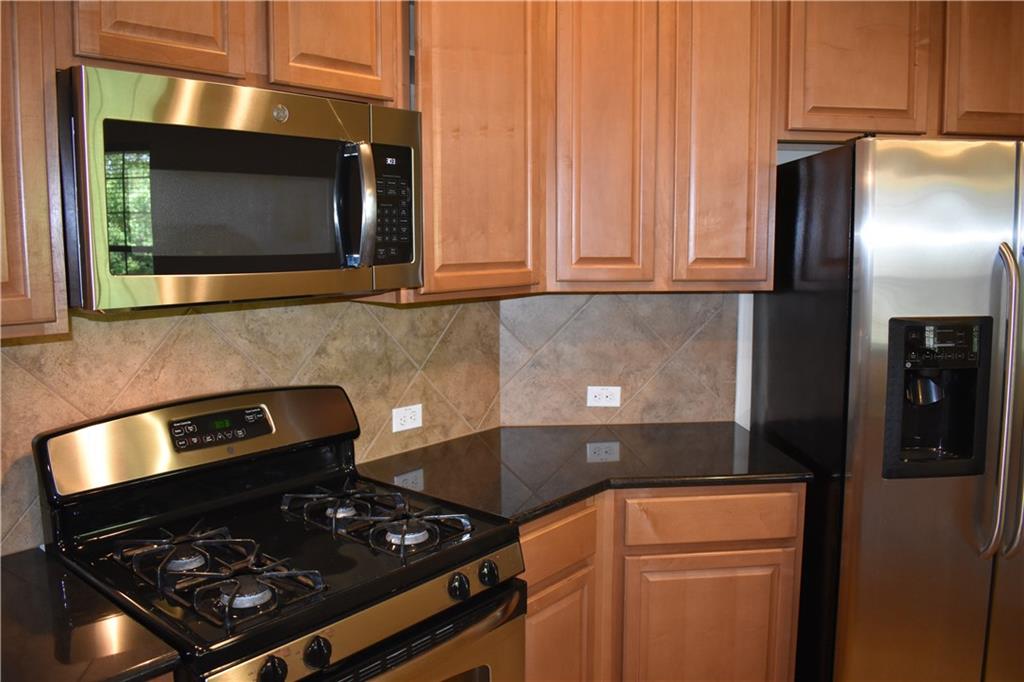 1310 West Parmer Lane, Unit 1503 Austin, TX 78727 - Photo 7 of 26 Kitchen featuring stainless steel appliances, dark stone counters, wood finish cabinets, and backsplash