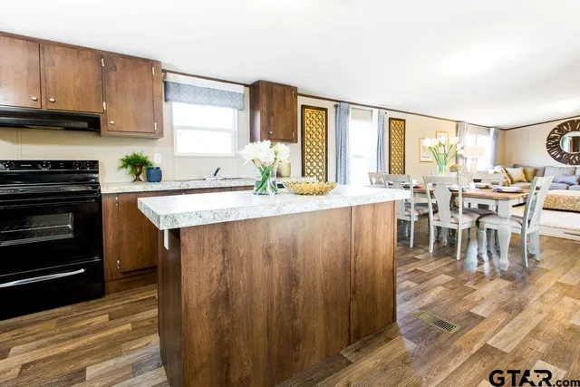 a open kitchen with granite countertop a stove top oven a sink and dining table with wooden floor