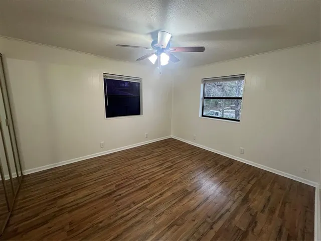 a view of an empty room with wooden floor and a ceiling fan
