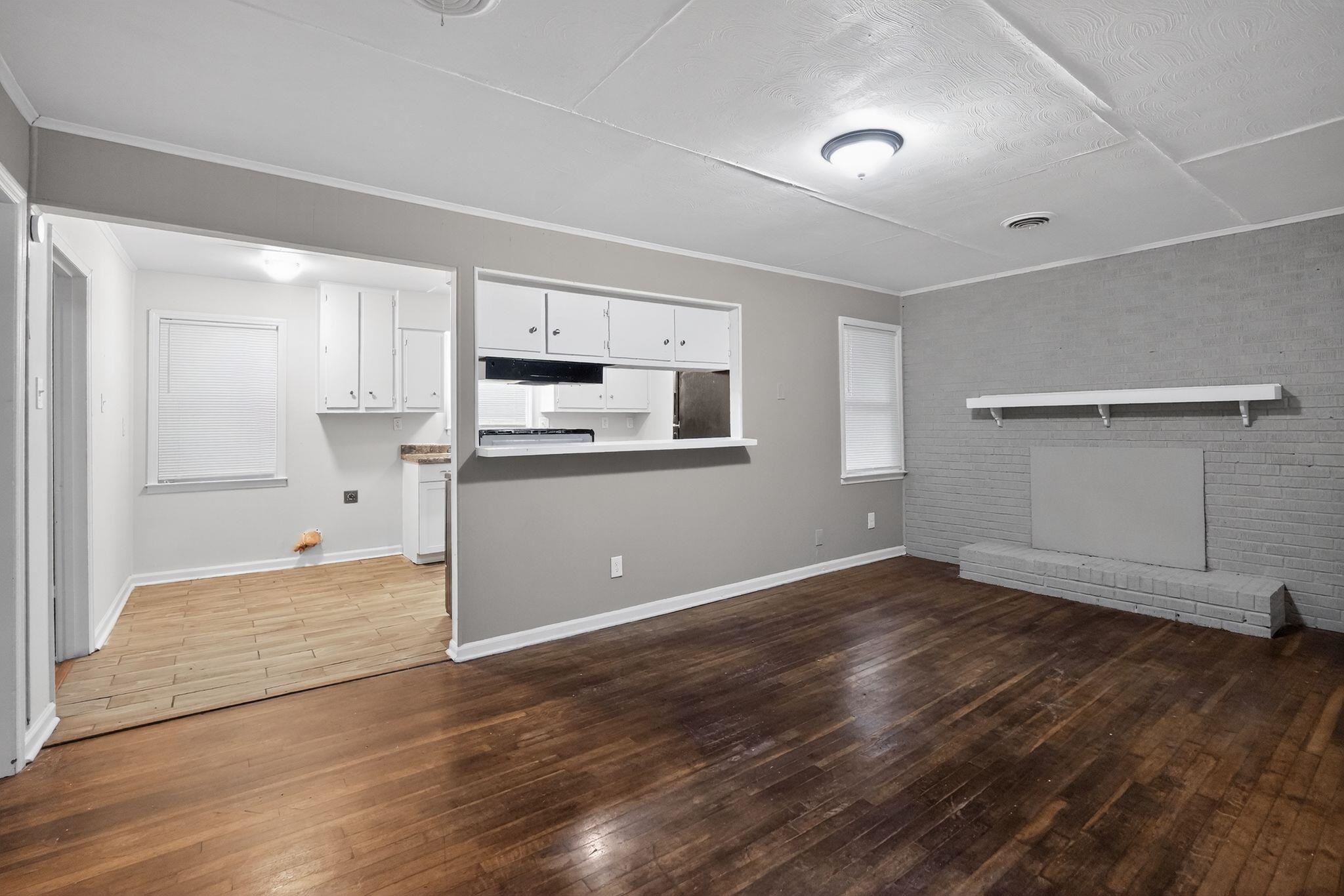 134 West Holmes Road Memphis, TN 38109 - Photo 16 of 30 Unfurnished living room with dark wood-type flooring, brick wall, crown molding, and a fireplace