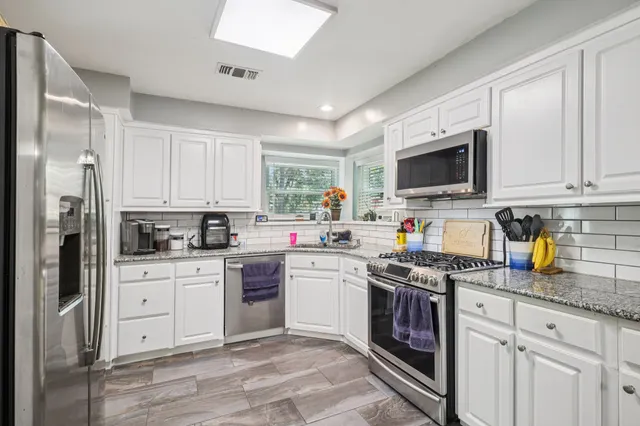 a kitchen with stainless steel appliances granite countertop a stove top oven a refrigerator a sink and dishwasher with white cabinets