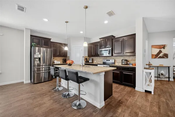 a kitchen with stainless steel appliances granite countertop a refrigerator a stove top oven a sink cabinets and wooden floor