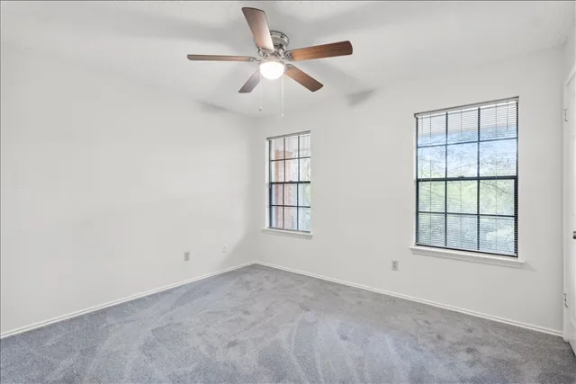 an empty room with ceiling fan and windows