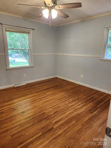 an empty room with wooden floor fan and windows